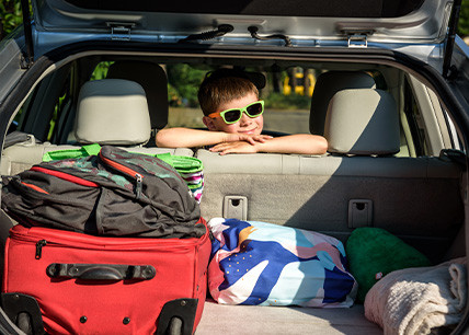 Enfant portant des lunettes de soleil appuyé à l'arrière d'une voiture chargée de valises et sacs pour les vacances d'été Enfant portant des lunettes de soleil appuyé à l'arrière d'une voiture chargée de valises et sacs pour les vacances d'été